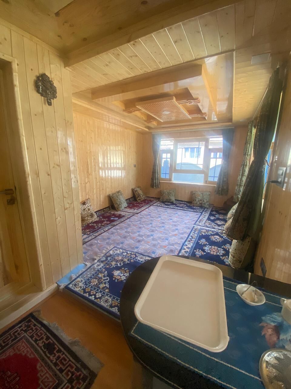 A wooden interior with a large window, a patterned rug, and a table with a tray.