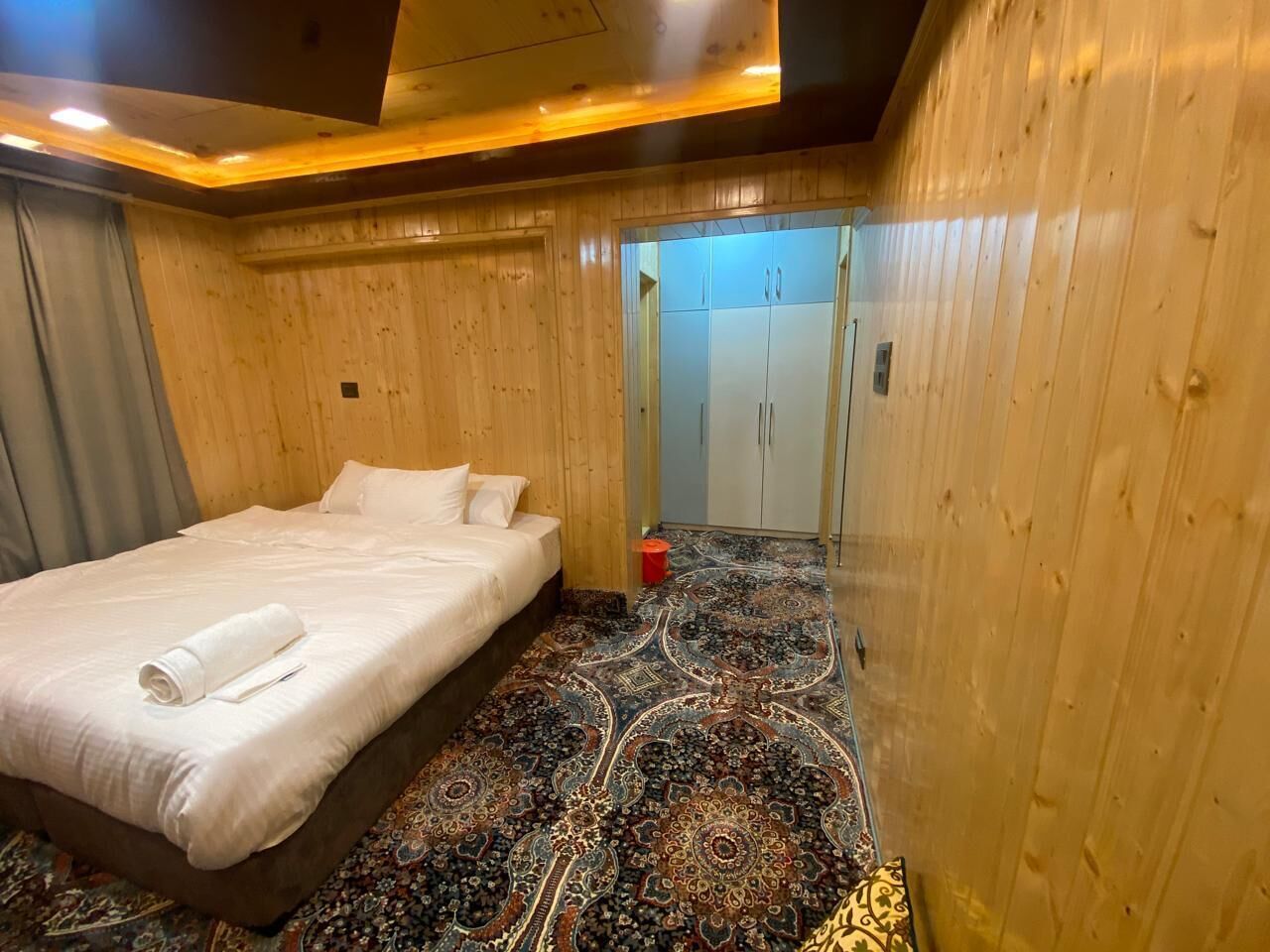 A hotel room with a bed, a patterned carpet, wooden walls, and a wardrobe.