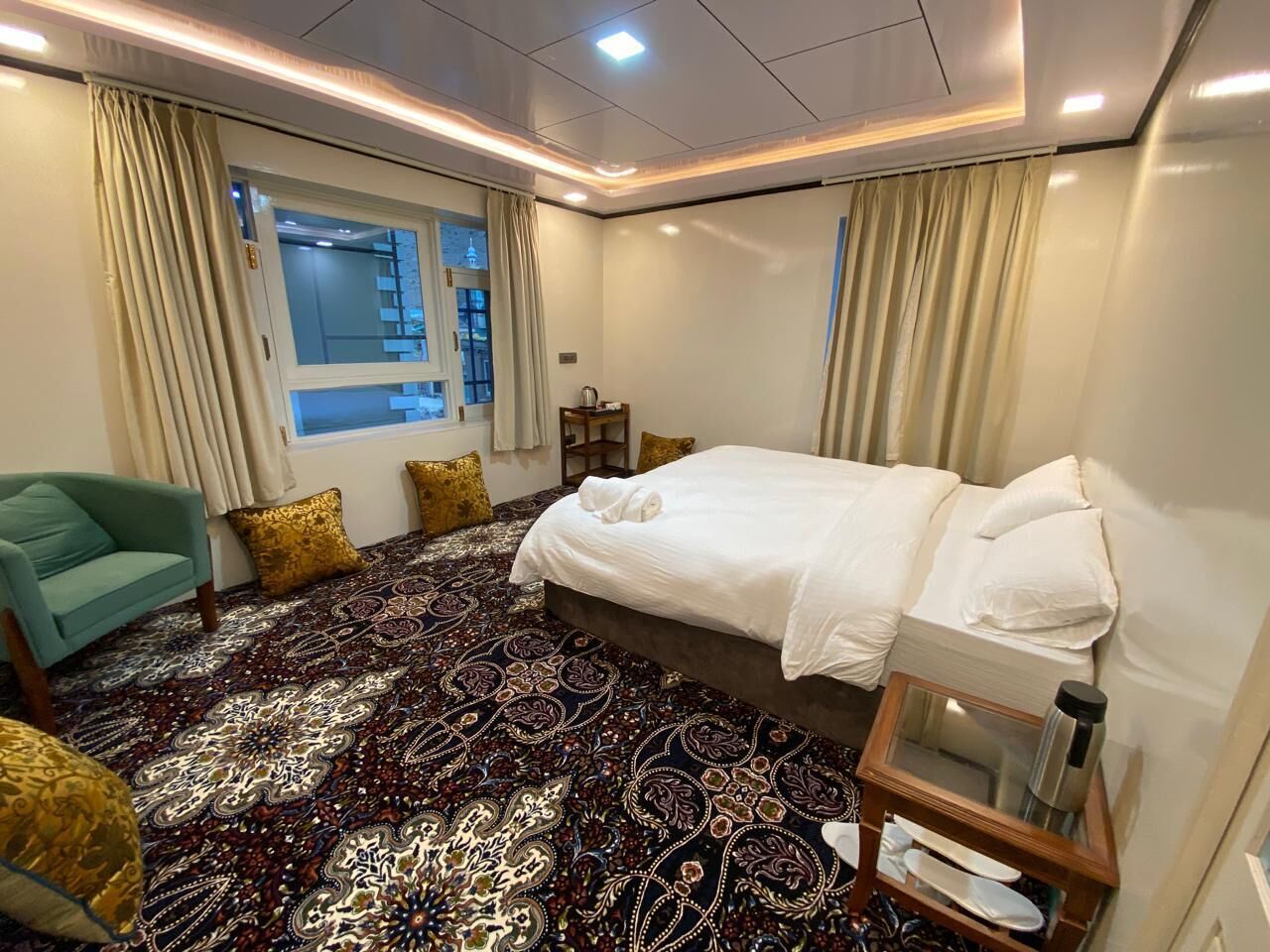 Una habitación de hotel con una cama grande, un sofá, una mesita y una ventana con cortinas.