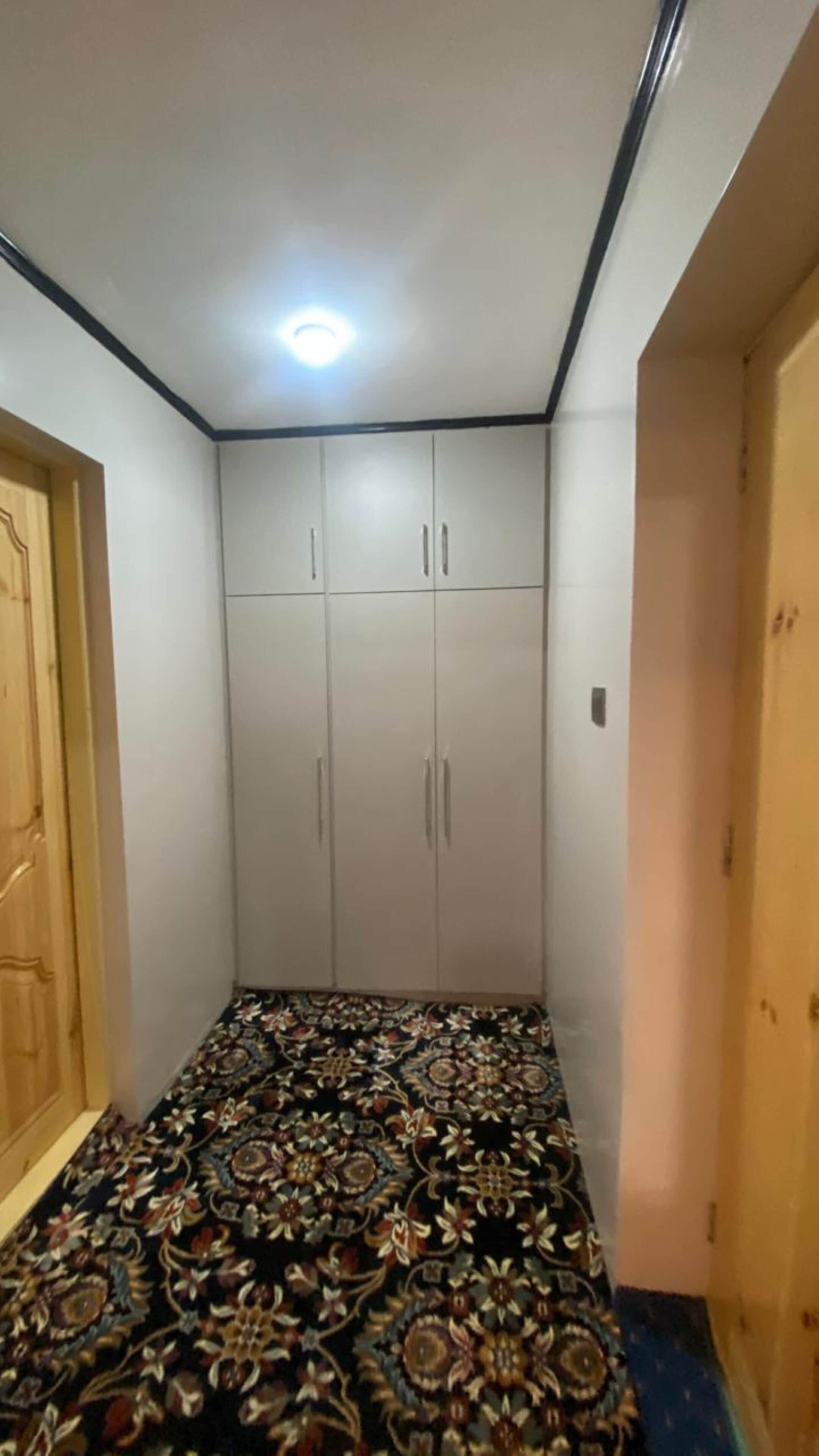 Quarto com carpete estampado, guarda-roupa de duas portas e uma luminária no teto.