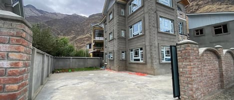 Un edificio de varios pisos con techo plano, entrada porticada y patio empedrado.