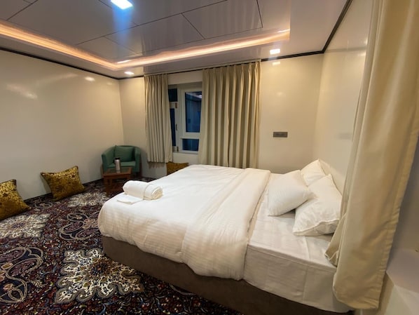 A hotel room with a large bed, a patterned carpet, a small table, and a chair.