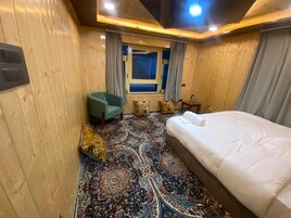 Una habitación con cama, ventana, silla y alfombra estampada.
