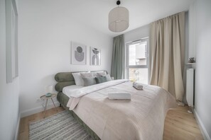 A modern bedroom with a bed, a bedside table, a lamp, and a window with curtains. - Kierbedzia Premium Apartament, Mokotów (Warszawa)