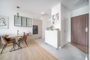 A modern kitchen with a dining area, featuring a wooden table, chairs, and a cabinet with a microwave. - Kierbedzia Premium Apartament, Mokotów (Warszawa)