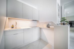 A modern kitchen with white cabinetry, a marble countertop, and a built-in oven. - Kierbedzia Premium Apartament, Mokotów (Warszawa)