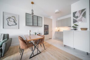 A modern kitchen with white cabinets, a dining table with chairs, and a hanging light fixture. - Kierbedzia Premium Apartament, Mokotów (Warszawa)