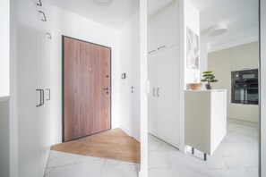A modern kitchen with white cabinetry, a wooden door, and a small potted plant. - Kierbedzia Premium Apartament, Mokotów (Warszawa)