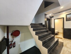 A modern staircase with a handrail, a fire extinguisher mounted on the wall, and a door leading to a room with a bed. - Oly Hotel Ruhaan Near New Delhi Railway  (New Delhi)