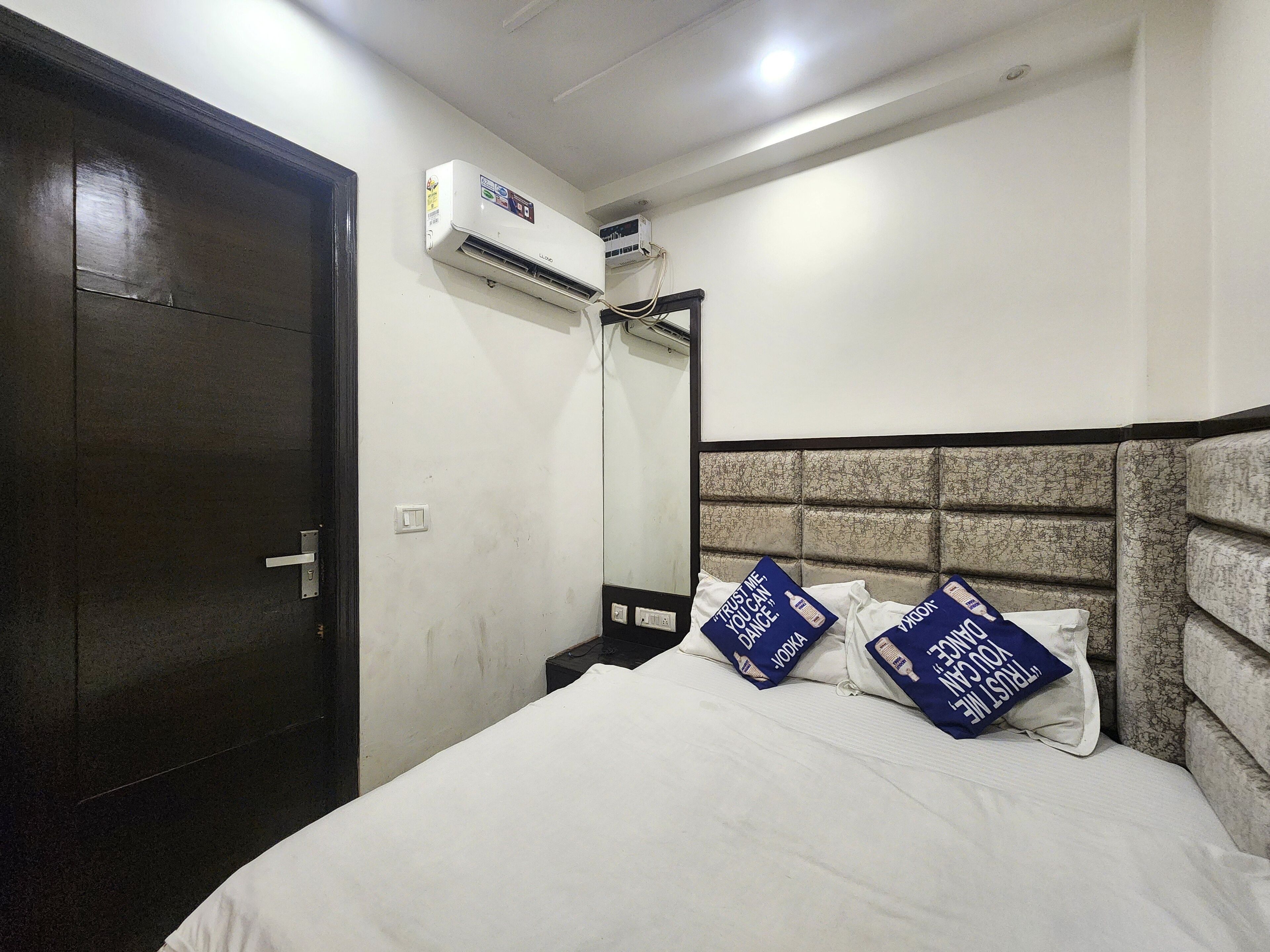 Una habitación de hotel con una cama, un armario, un equipo de aire acondicionado y un espejo.