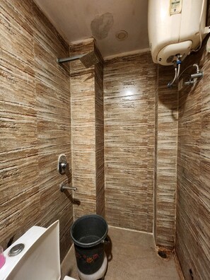 A bathroom with a shower, a toilet, and a bucket. - Oly Hotel Ruhaan Near New Delhi Railway  (New Delhi)