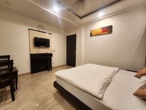 A hotel room with a bed, a TV mounted on the wall, a desk with a chair, and a door. - Oly Hotel Ruhaan Near New Delhi Railway  (New Delhi)