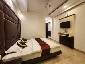 A bedroom with a bed, a TV mounted on the wall, and a door leading to another room. - Oly Hotel Ruhaan Near New Delhi Railway  (New Delhi)