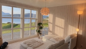 A room with a white sofa, a large window with a view of the outdoors, and a hanging light fixture.