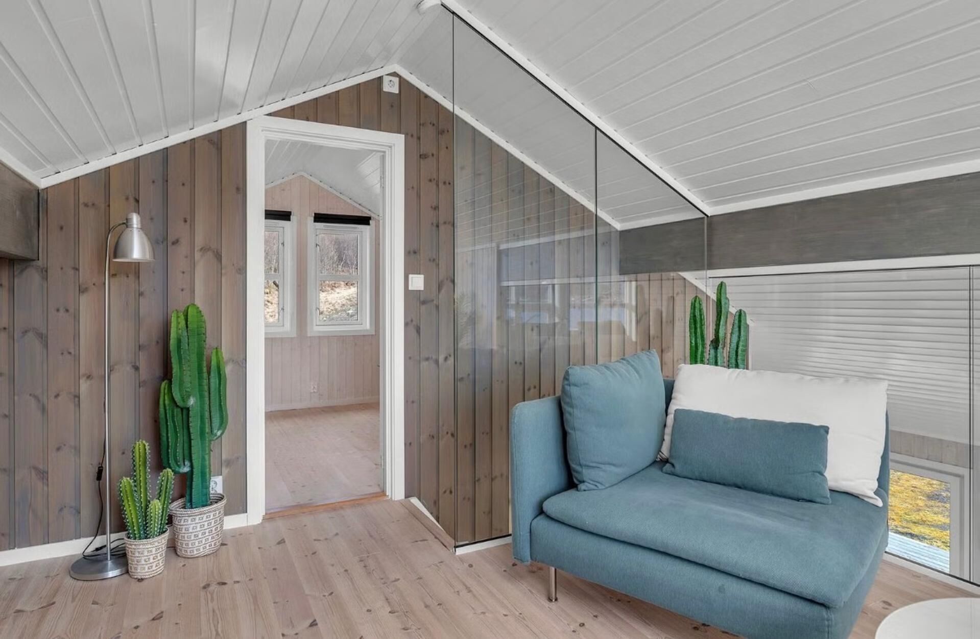 A modern interior with a wooden floor, a blue sofa, and two potted cacti.