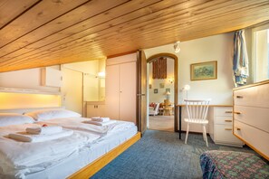 Habitació d'hotel amb un llit, una taula de treball, una cadira i una vista per una porta oberta.