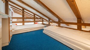 A room with two beds, a blue carpet, wooden beams, and a white ceiling.