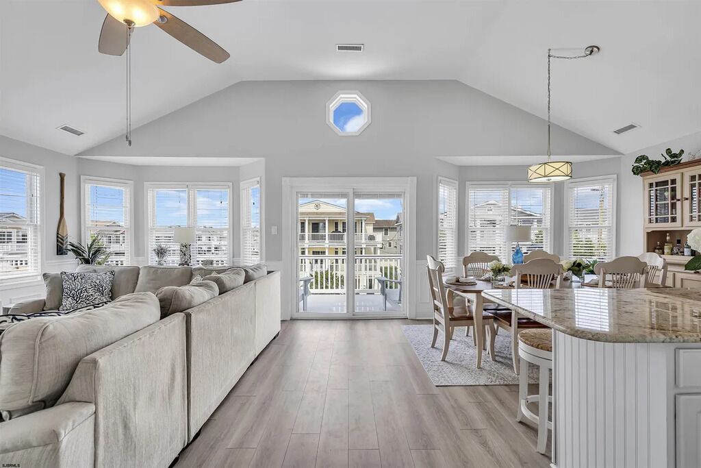 A spacious living room with a large sofa, a dining area with a table and chairs, and a kitchen with a central island.