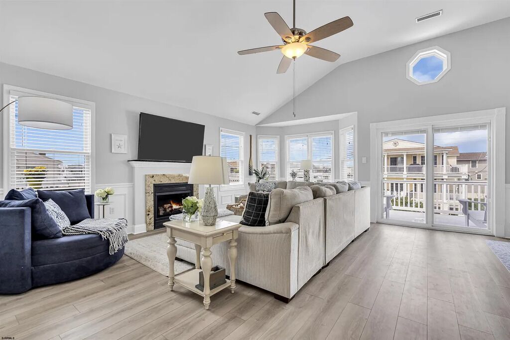 A spacious living room with a fireplace, a ceiling fan, and a large window offering a view of the outside.