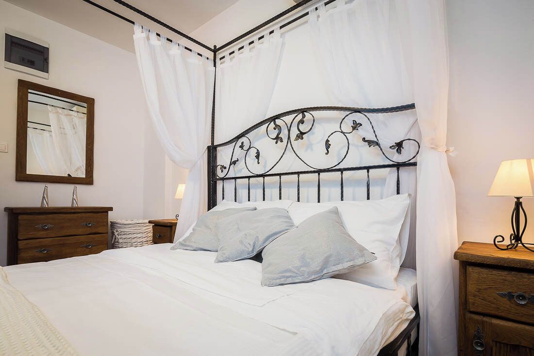 Een net opgemaakt bed met witte lakens en een metalen hoofdbord, met aan beide kanten houten nachtkastjes en lampen.