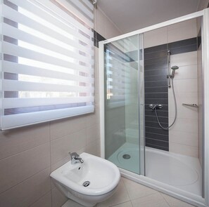 Un bagno moderno con doccia vetrata, un bidet e una finestra con persiane.