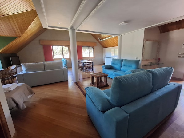 A spacious living area with a high ceiling, wooden beams, and a dining area with a table and chairs.