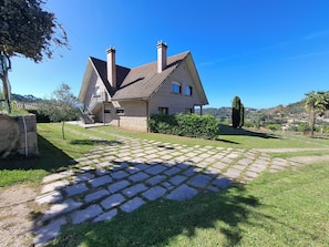 A house with a stone facade, a tiled roof, and a paved driveway leading to a staircase.