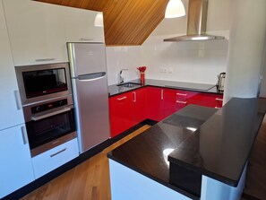 A modern kitchen with stainless steel appliances, red cabinets, and a black countertop. - Villaza Cottage (Gondomar)