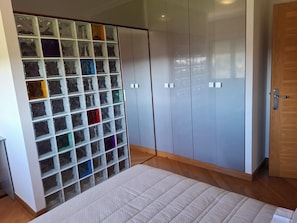 A bedroom with a bed, a wardrobe, and a storage unit with transparent drawers.
