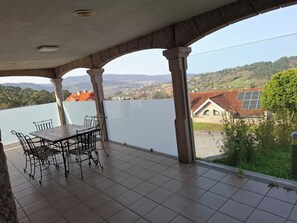 A covered outdoor area with a table and chairs, a view of a lake, and a house with solar panels. - Villaza Cottage (Gondomar)