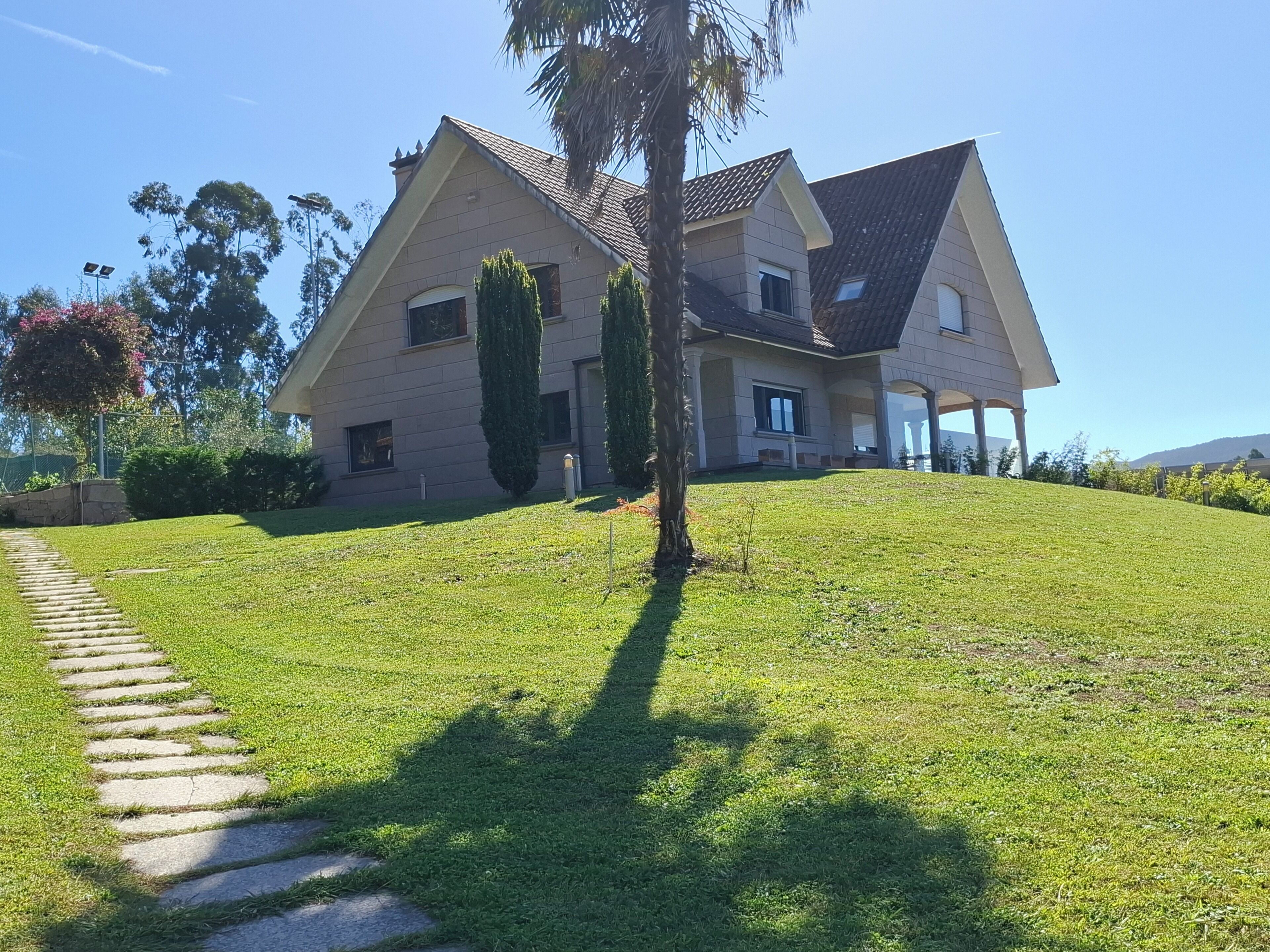 A two-story house with a sloped roof, a well-maintained lawn, and a stone pathway leading to the entrance.