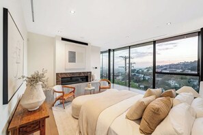 Une chambre moderne avec un grand lit, une cheminée, un bureau et une vue sur la ville.