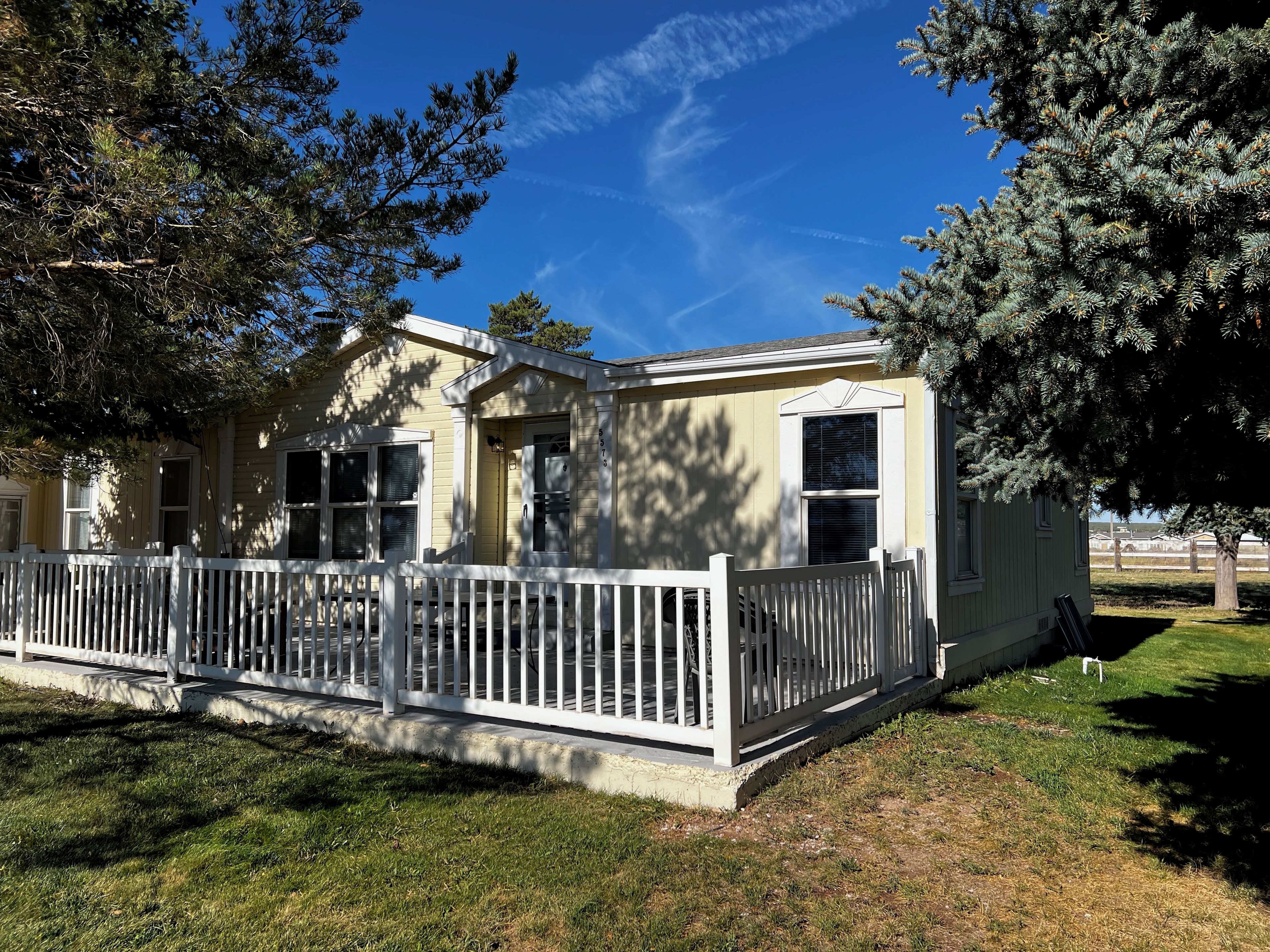 A single-story house with a white picket fence, a covered porch, and a clear blue sky.