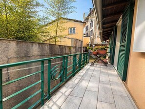 A narrow outdoor corridor with a green metal railing, potted plants, and a tiled floor.