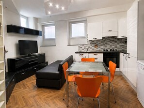 A compact kitchen with a dining area, a flat-screen TV, and a sofa.