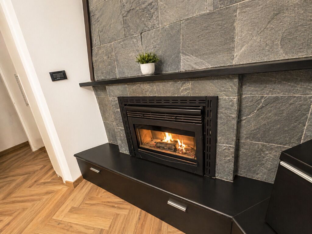 Una chimenea moderna con un fondo de pared de piedra, una pequeña planta en maceta encima y un suelo de madera con patrón de espiga.