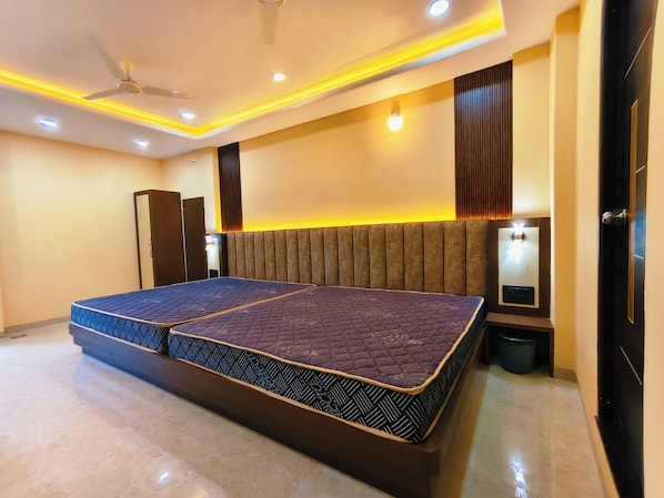 A modern bedroom with a large bed, recessed ceiling lights, a ceiling fan, and a wall-mounted light fixture.