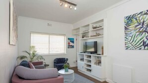 Ein Wohnzimmer mit einer Couch, einem Fernseher, einem Bücherregal und einer Pflanze.
