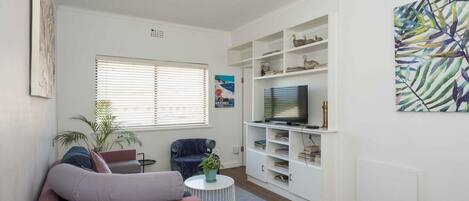 A living room with a sofa, a television, a bookshelf, and a plant.