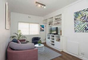 A living room with a sofa, a television, a bookshelf, and a plant. - Stylish Gardens Apt Views, Steps from Kloof Street (Cape Town)