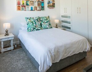 A bedroom with a bed, nightstands, a lamp, a wardrobe, and a wall with a poster. - Stylish Gardens Apt Views, Steps from Kloof Street (Cape Town)