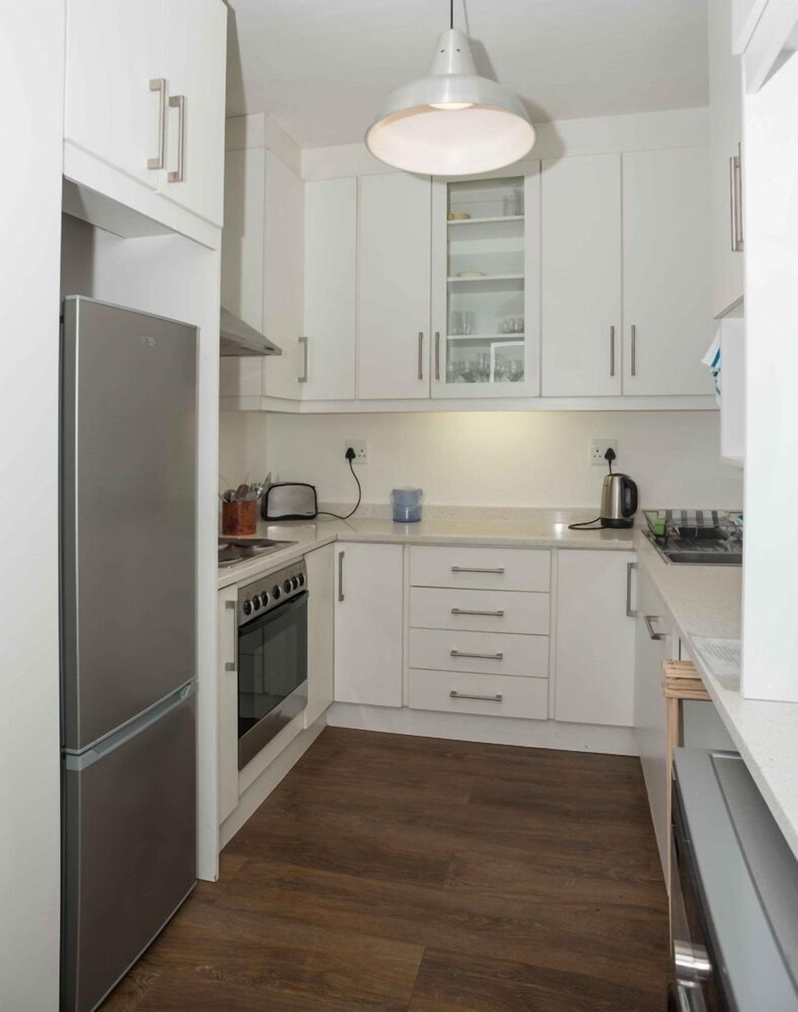 A compact kitchen with white cabinets, a stainless steel refrigerator, a stove, and a microwave.