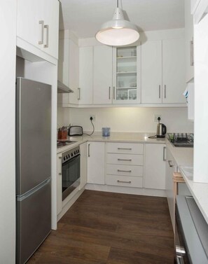 A compact kitchen with white cabinets, a stainless steel refrigerator, a stove, and a microwave. - Stylish Gardens Apt Views, Steps from Kloof Street (Cape Town)