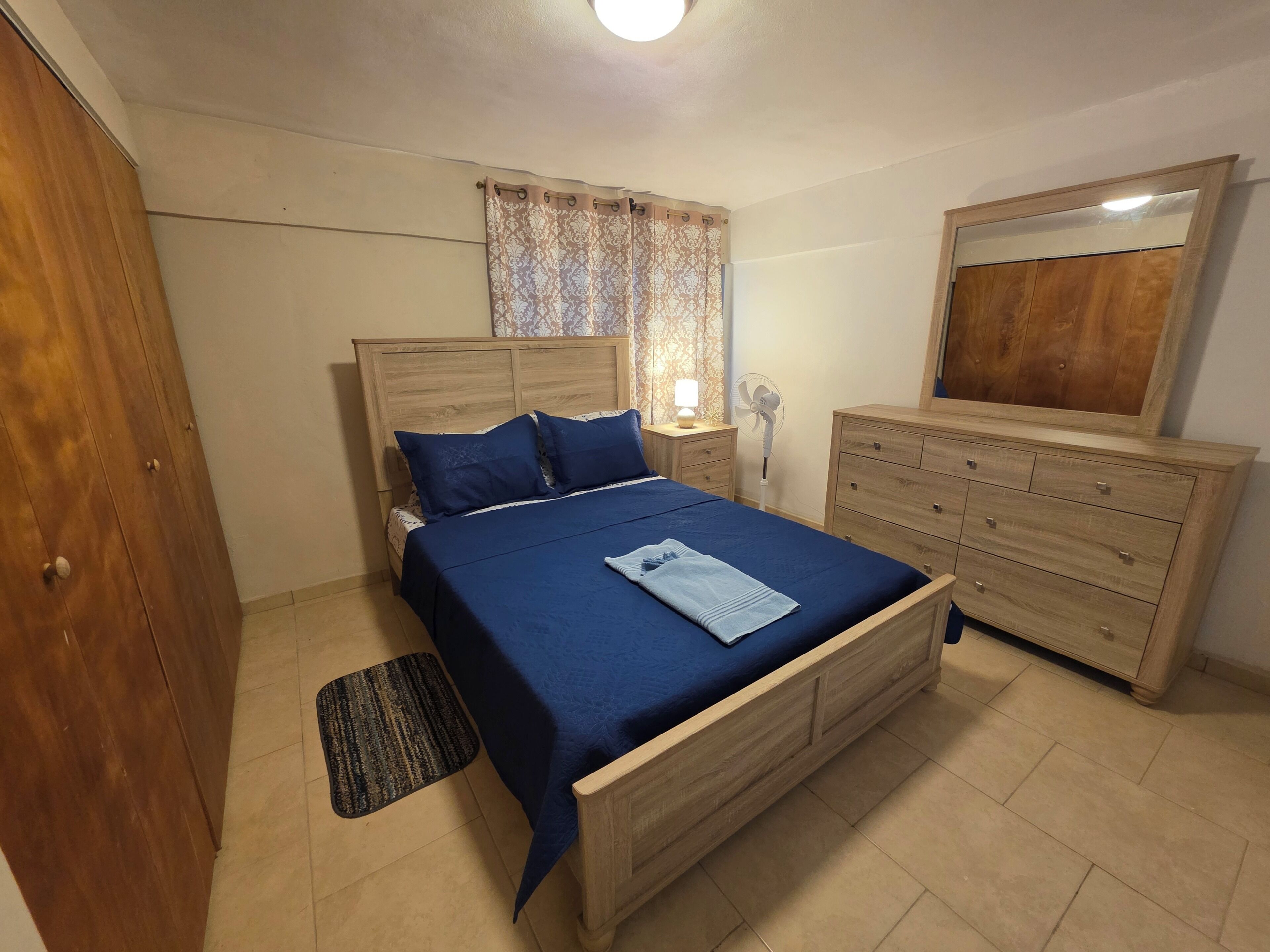 Un dormitorio con una cama de madera, una mesita de noche con una lámpara, un aparador y un espejo.
