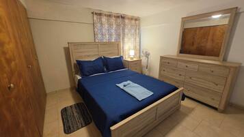 Un dormitorio con una cama de madera, una mesita de noche con una lámpara, un aparador y un espejo.