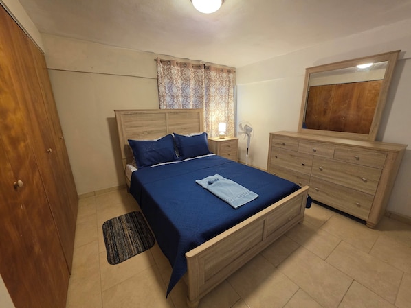 A bedroom with a wooden bed, a nightstand with a lamp, a dresser, and a mirror.