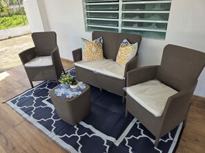 A patio area with wicker furniture, including two chairs and a sofa, a round table with a plant, and a patterned rug.