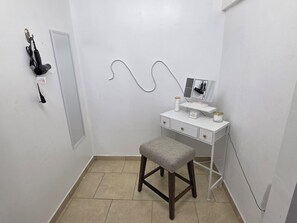 A small, white vanity with a mirror, a stool, and a shelf with personal items.