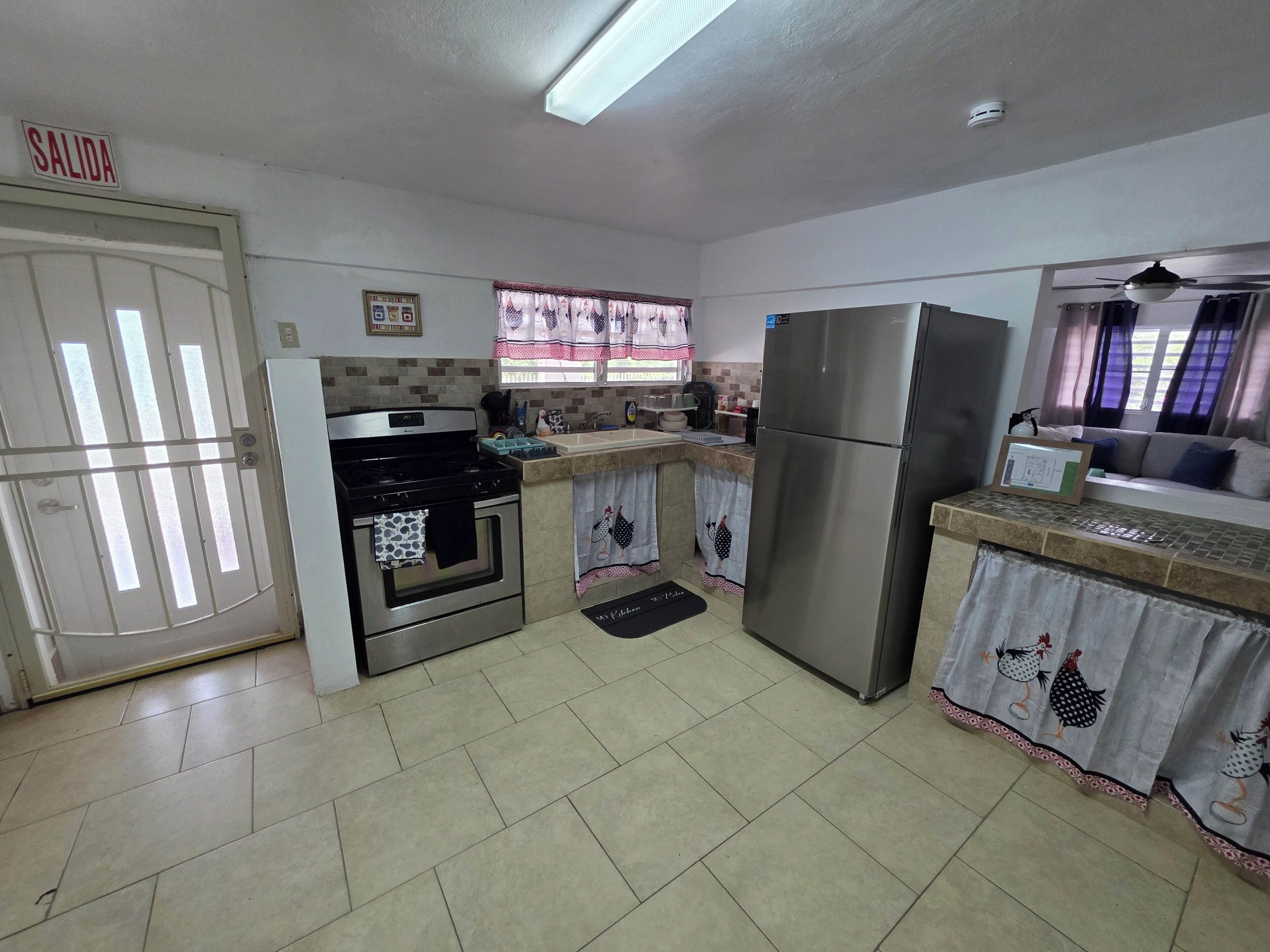 Una cocina con estufa, horno, refrigerador y una ventana con cortinas.