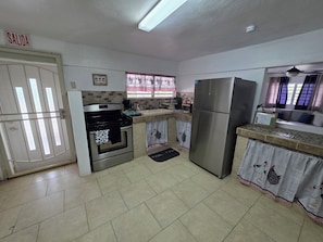 A kitchen with a stove, oven, refrigerator, and a window with curtains.